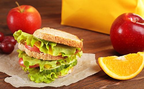 Sandwich mit grünem Salat, Orangenscheibe und roten Äpfeln zum Frühstück