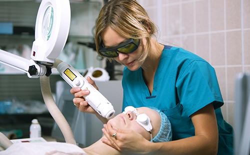 Kosmetikerin behandelt das Gesicht des Patienten mit einem Laser