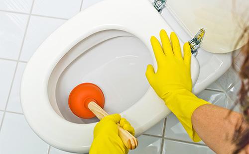 Hände in gelben Handschuhen waschen die Toilette mit einem Kolben.
