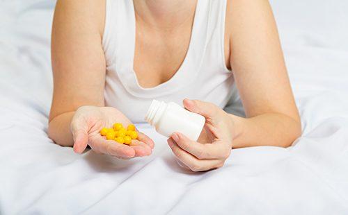 Ang babaeng nasa kama ay may hawak na dilaw na tabletas