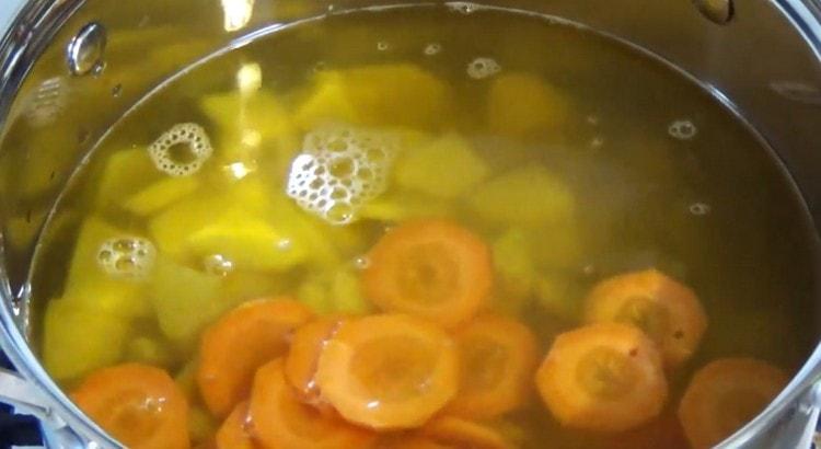 Fügen Sie Kartoffeln und geschnittene Karotten der kochenden Suppe hinzu.